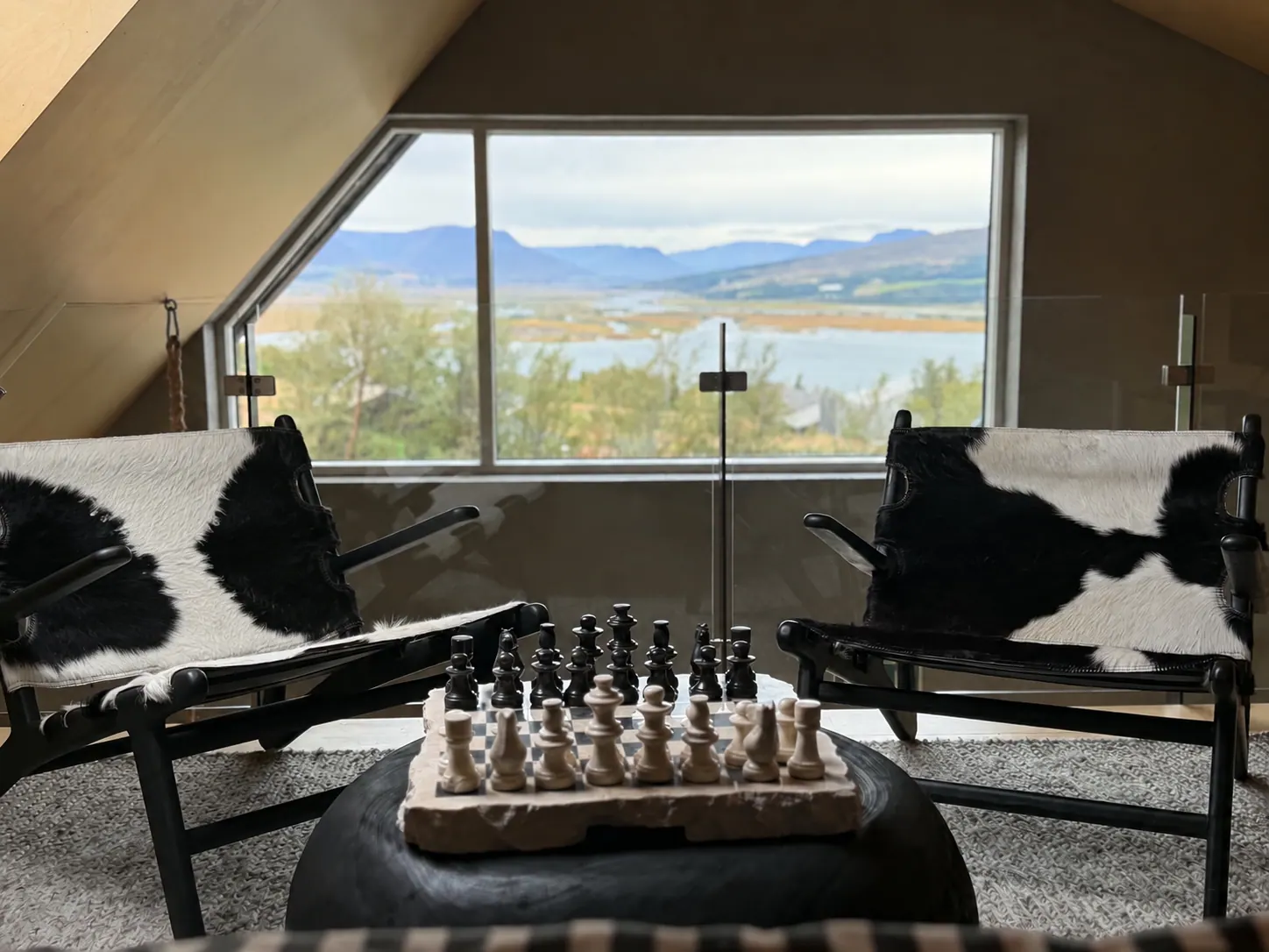 Apartment 15B: Lounge chairs and chess set by a window with a fjord view